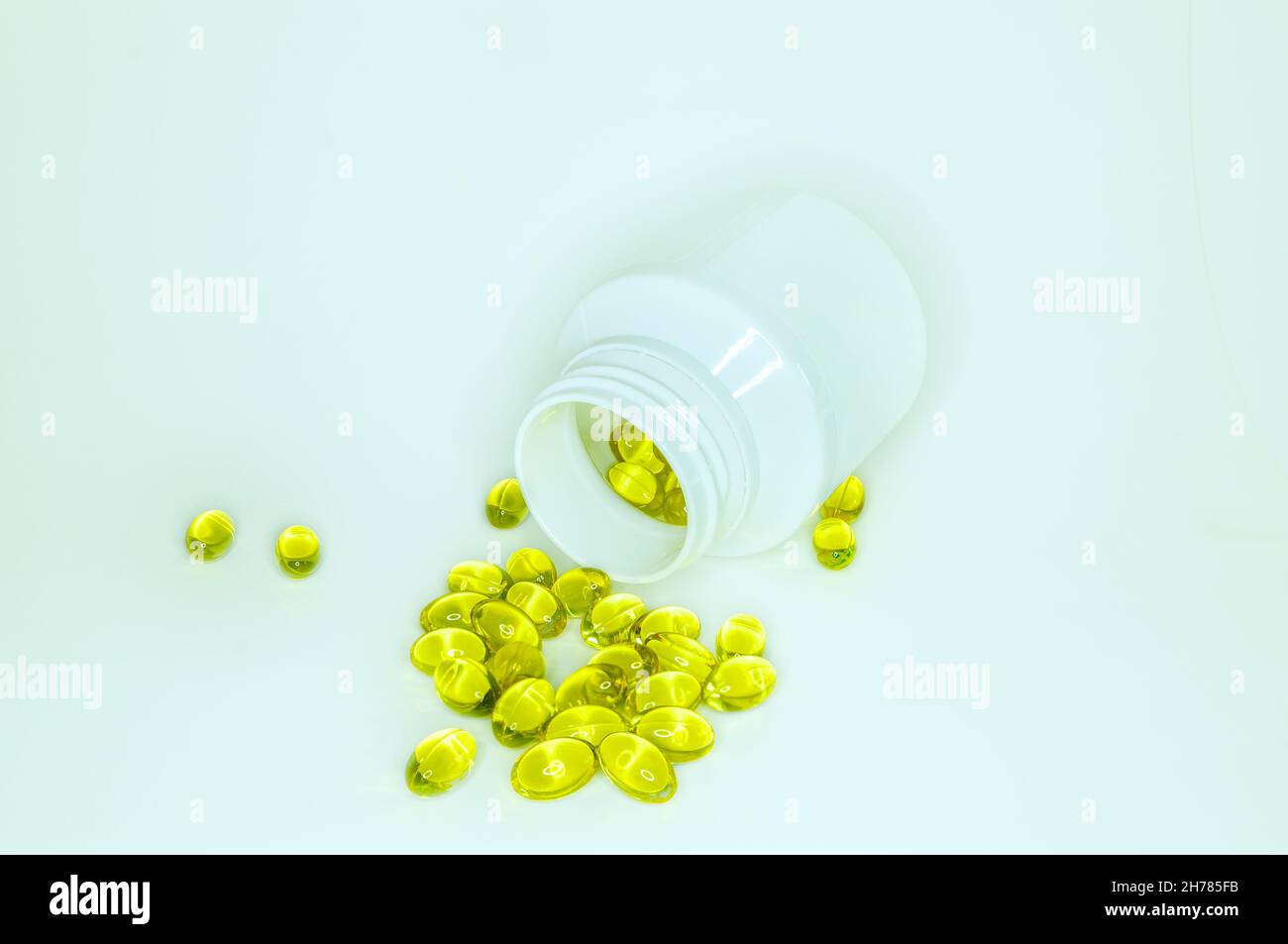 Golden transparent capsules of pharmacology product scattered from white plastic jar on white background. Cosmetology or medicine concept, disease pre Stock Photo