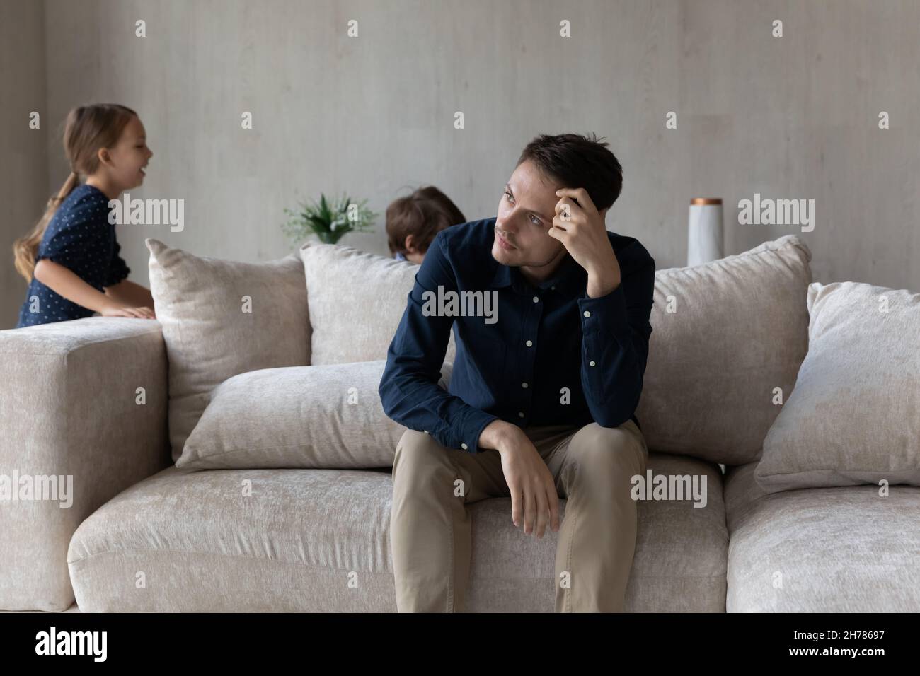 Tired pensive man sit on sofa fatigued due noisy kids Stock Photo