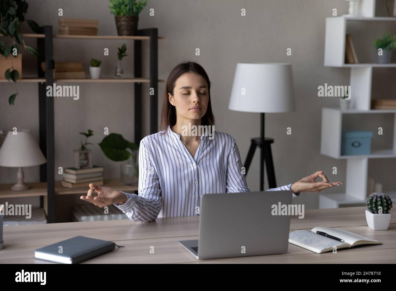Relaxed peaceful young business woman meditating in office. Stock Photo