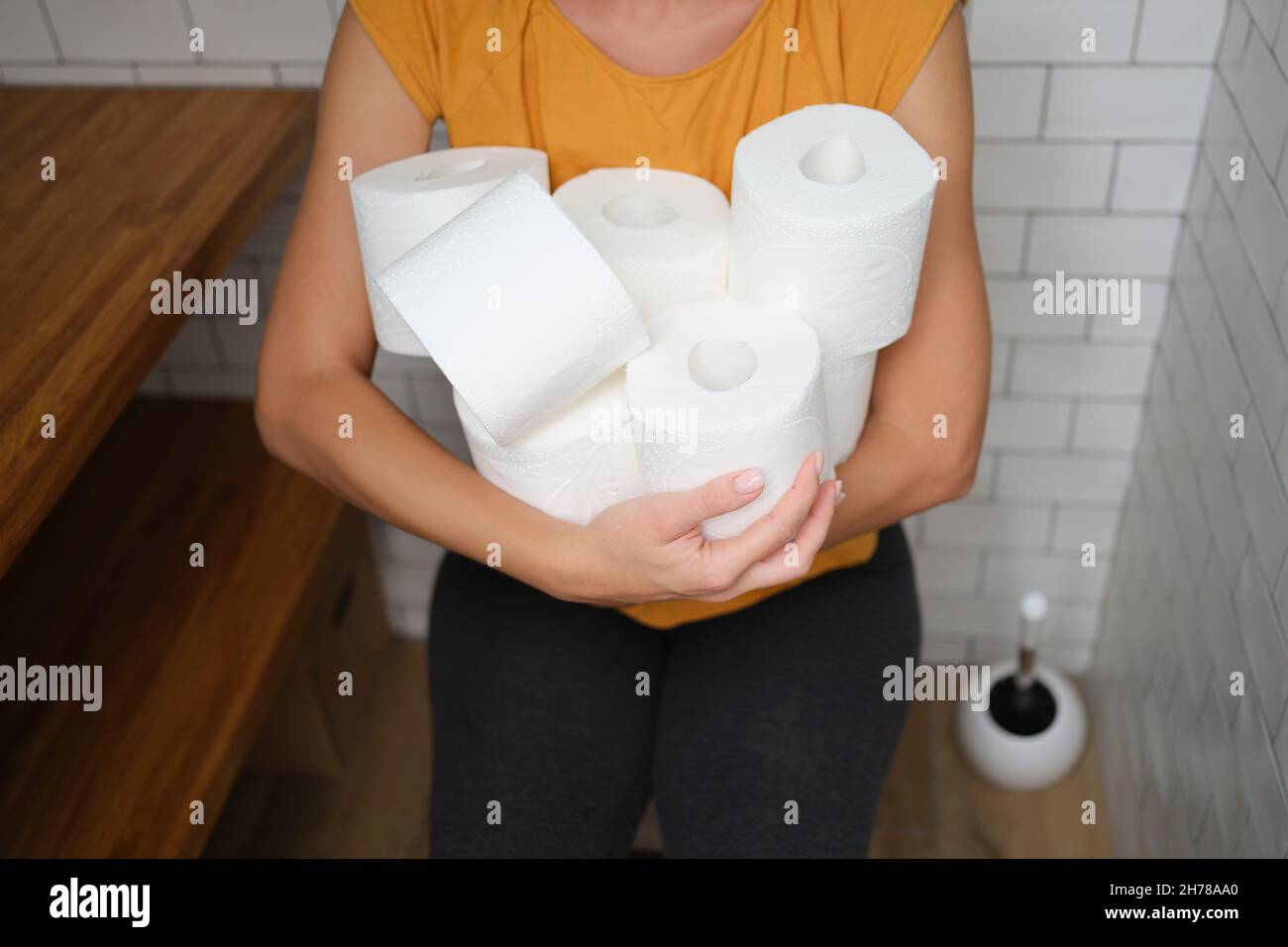 Woman sitting on toilet with rolls of toilet paper Stock Photo