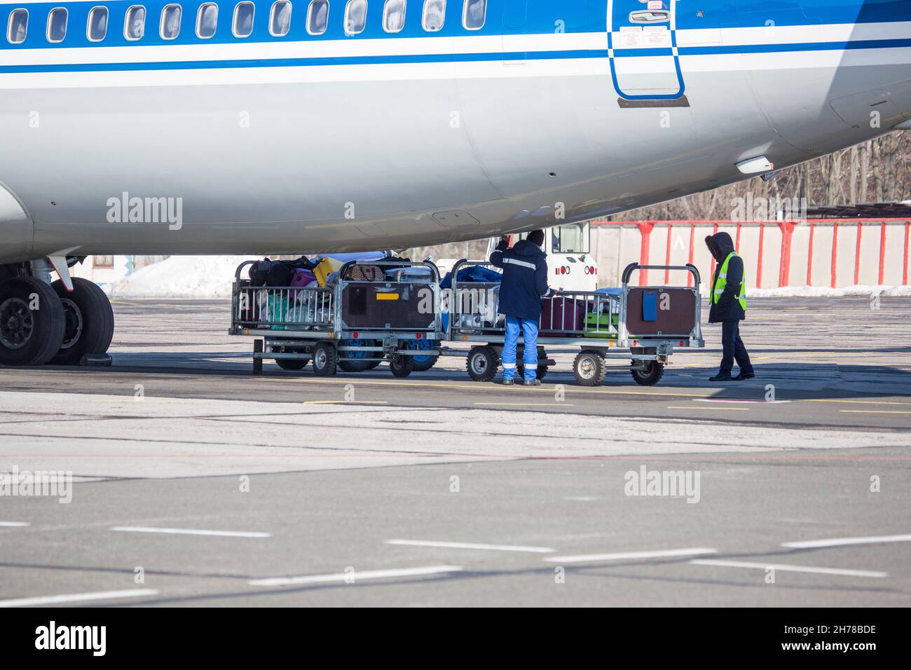 baggage loading at airport in winter. Luggage in carts near aircraft in winter. Passenger aircraft in winter at airport loaded baggage before departur Stock Photo