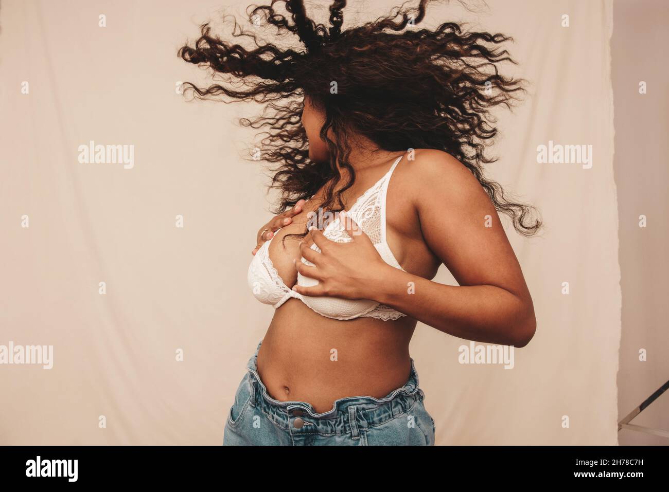 Young woman whipping her hair and embracing her body in a studio. Confident young woman having fun against a studio background. Body positive young wo Stock Photo