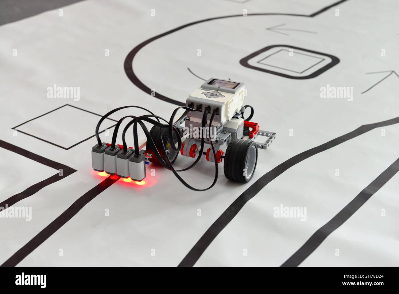 Programmable robot with wheels and red lights driving on paper road. robotic car with line follow Stock Photo