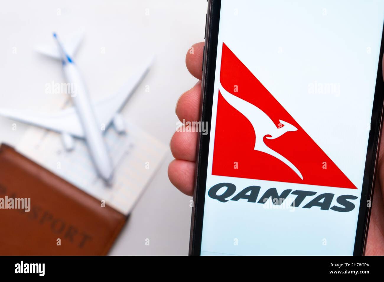 Qantas Airline application on the screen of mobile phone in mans hand. Passport, boarding bass are next to a white plane on the background. November 2021, San Francisco, USA Stock Photo