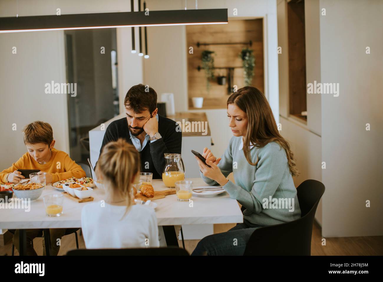 Family using mobile phones while having breakfast at dining table at the apartment Stock Photo