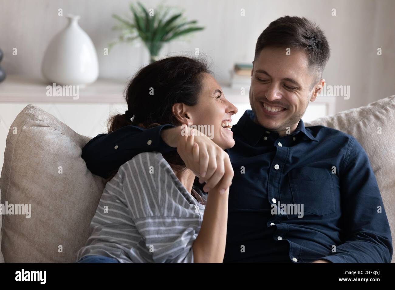 Young 30s peaceful couple hugging relaxing on sofa enjoy conversation Stock Photo