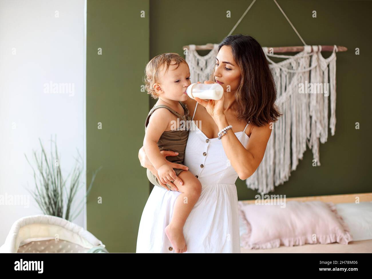 Young loving mother holding child hands and feeding baby boy son with milk  from bottle, beautiful mom standing in cozy boho bedroom at home and enjoyi  Stock Photo - Alamy