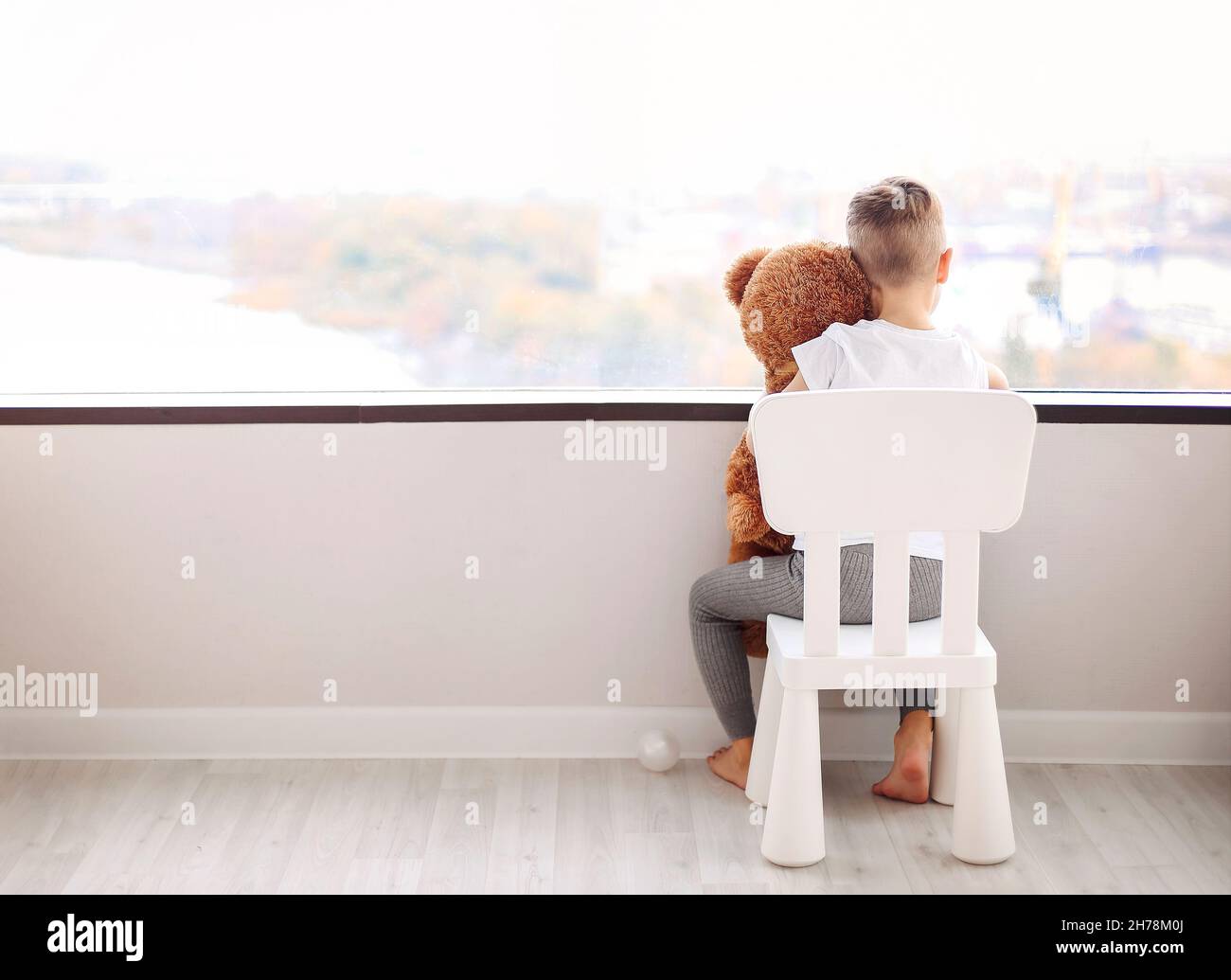 Rear view of little boy with teddy bear sitting on chair and looking ...