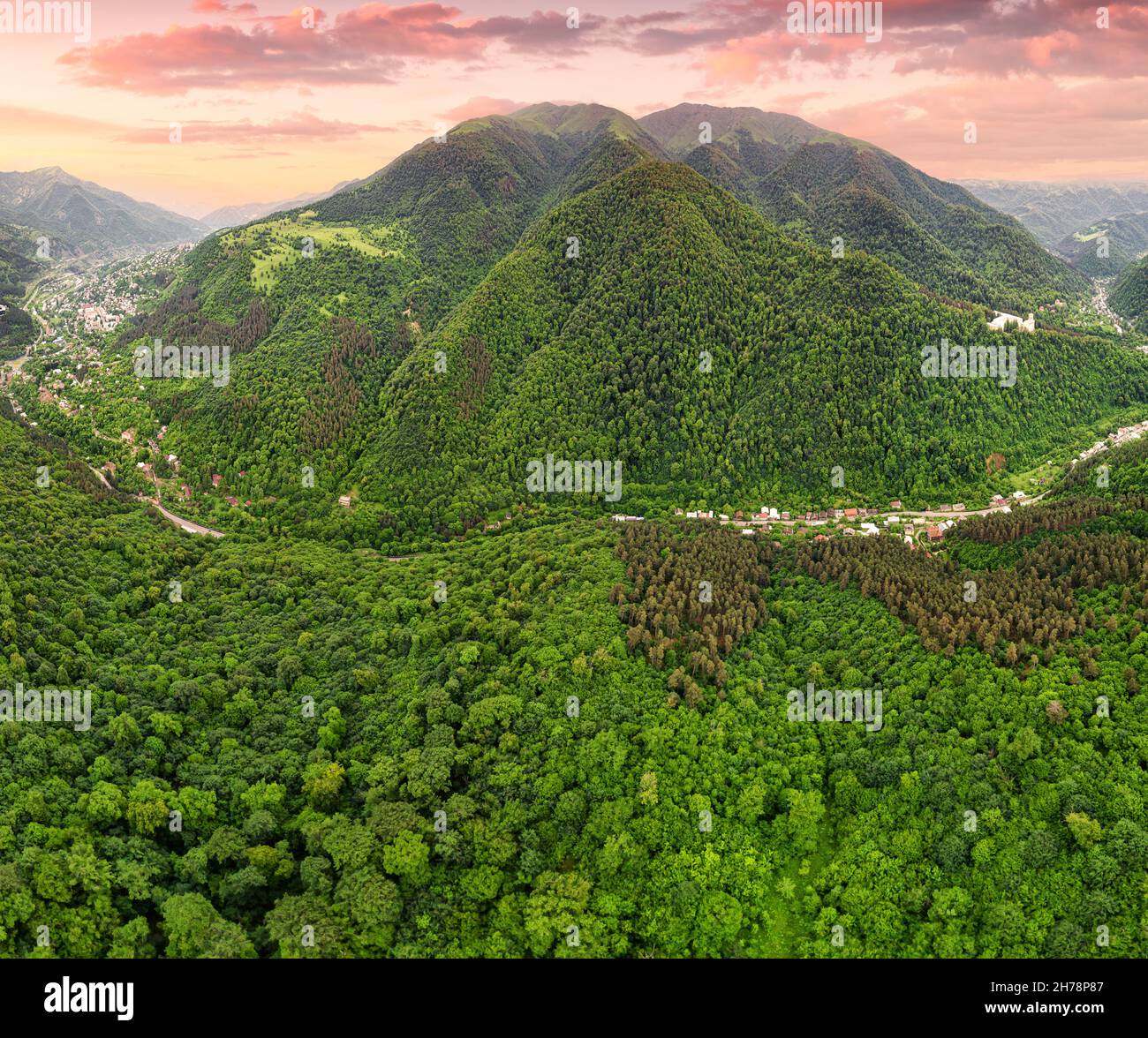 Drone view of a mountain valley with dense forests and a road along ...