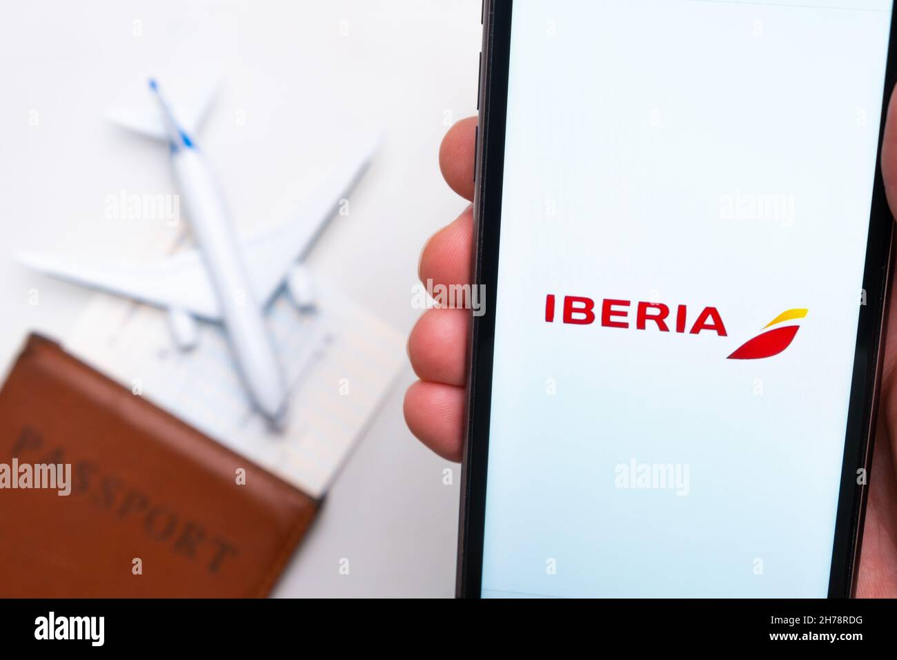 Iberia Airline application on the screen of mobile phone in mans hand. Passport, boarding bass are next to a white plane on the background. November 2021, San Francisco, USA Stock Photo
