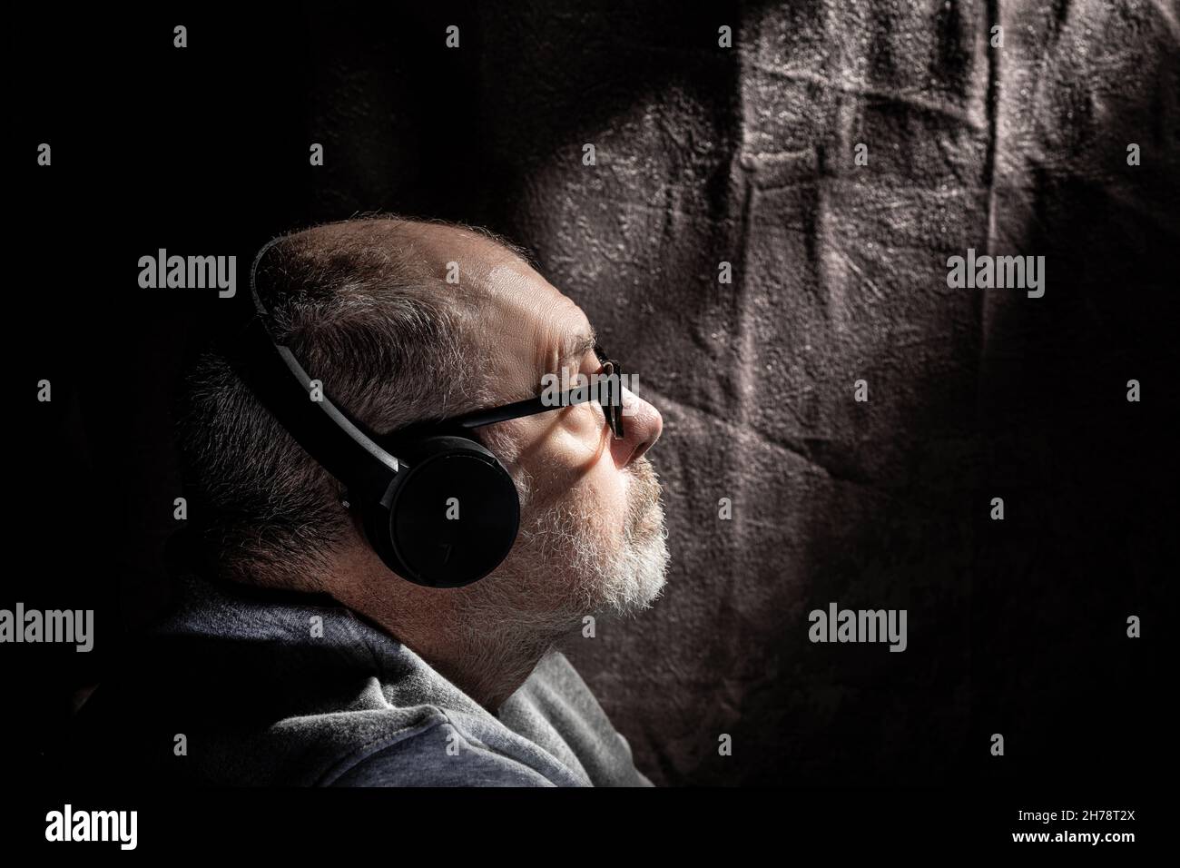 Low key profile portrait of a grey haired male listening to music through head phones Stock Photo