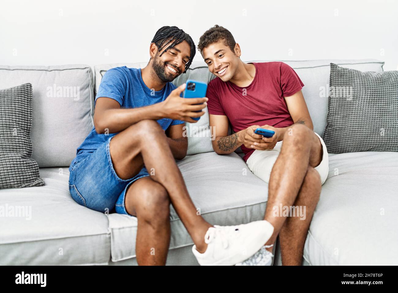 Two men friends using smartphone sitting on sofa at home Stock Photo
