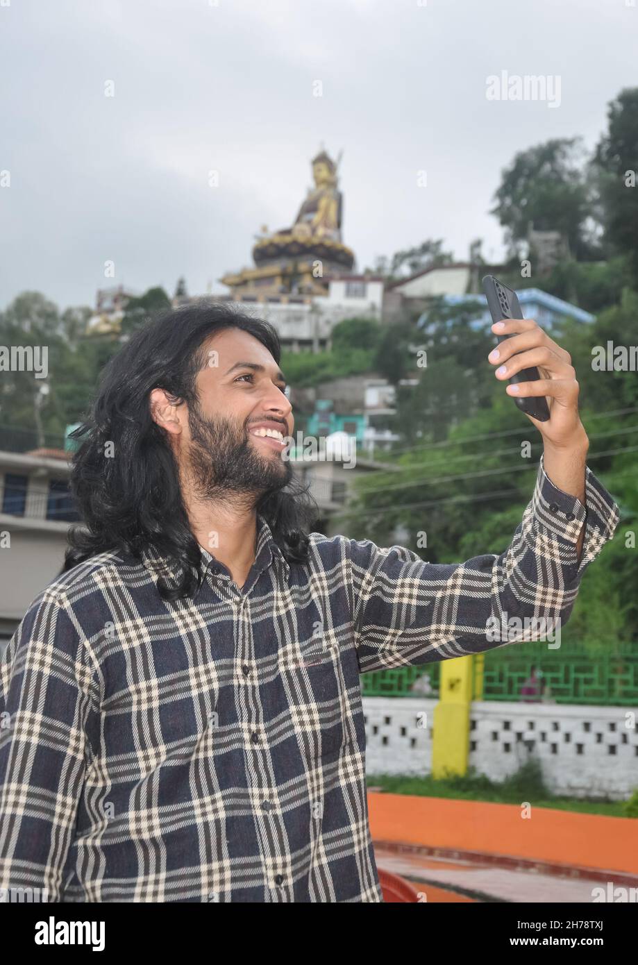 A charming long haired and bearded young guy smiling with taking selfie ...