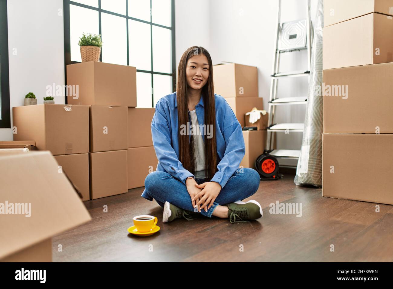 Young chinese girl sitting on the floor at new home with a happy and ...
