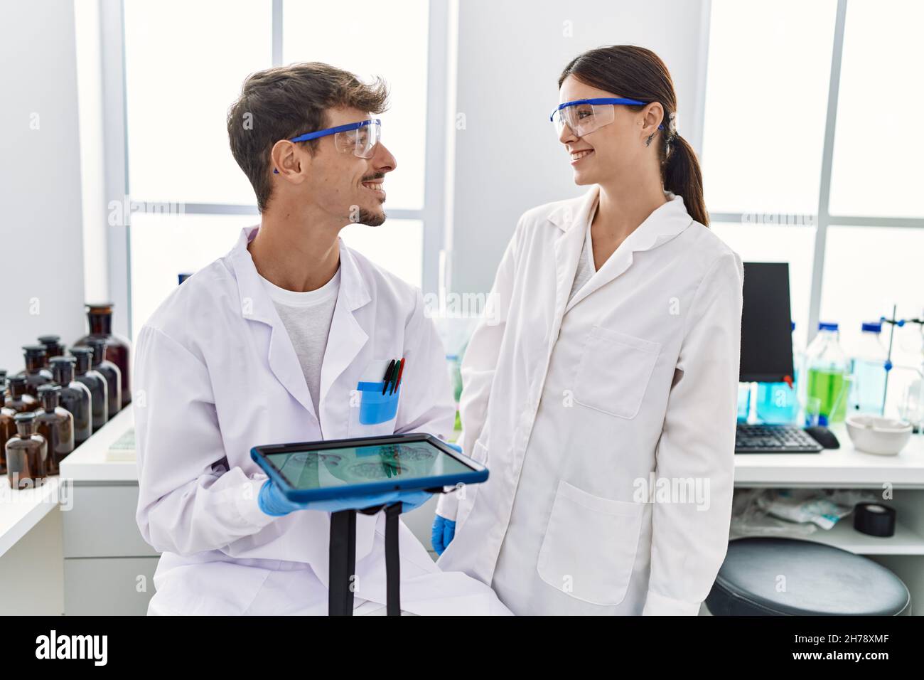 Man and woman partners wearing scientist uniform using touchpad with