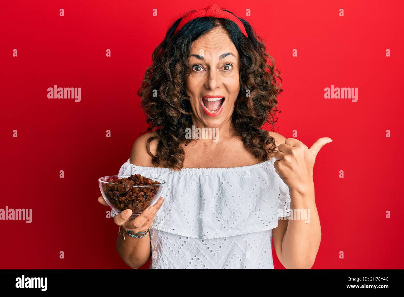 Middle age hispanic woman holding bowl with raisins pointing thumb up ...