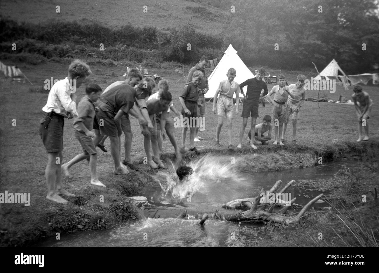1939, historical, summer scout camp, Ringmore, Devon, England, UK, outside in a field watched by other cub scouts, a boy making a splash as he takes a dip in the stream. Stock Photo