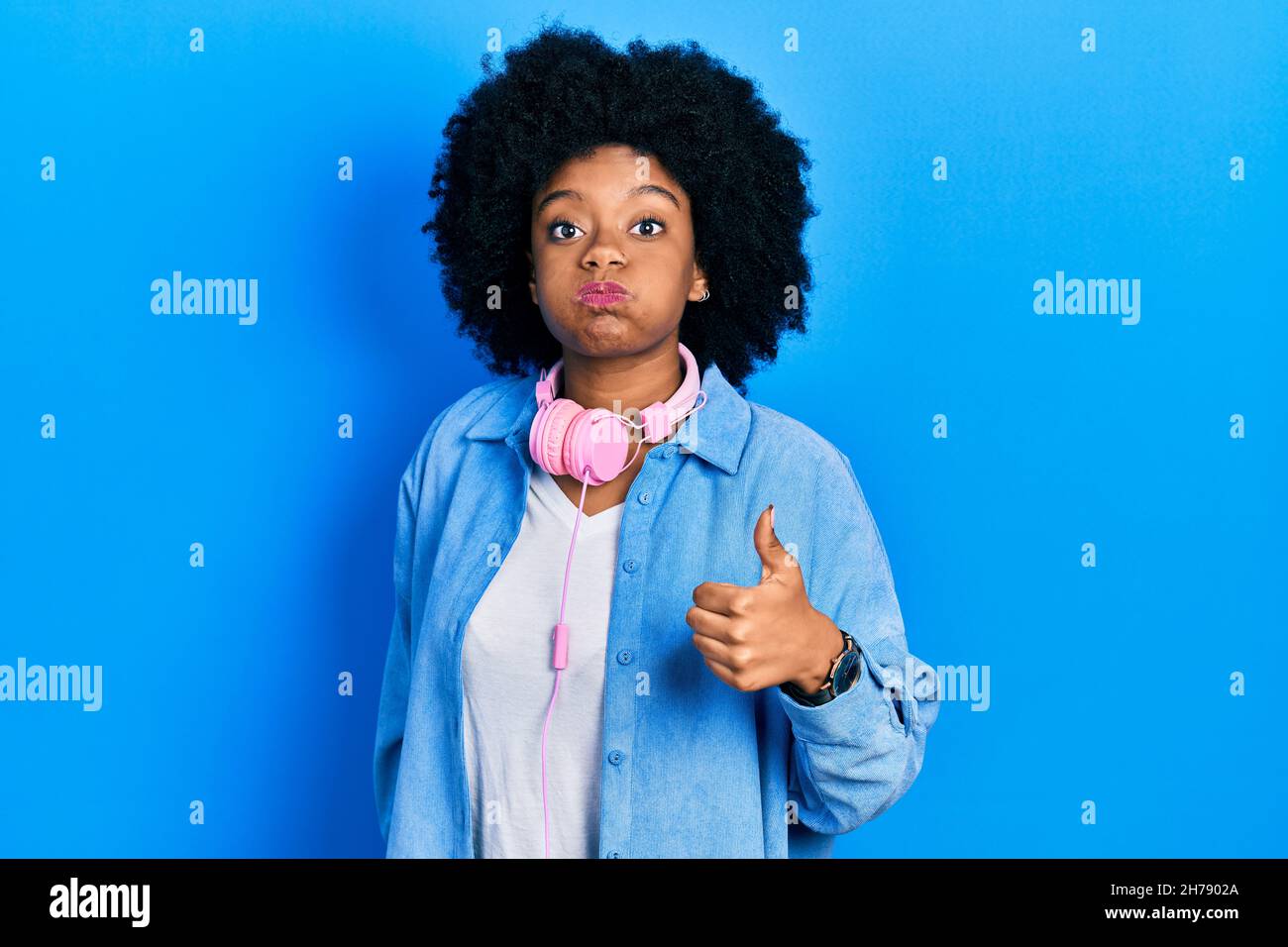Young african american woman wearing headphones doing thumbs up positive gesture puffing cheeks with funny face. mouth inflated with air, catching air Stock Photo