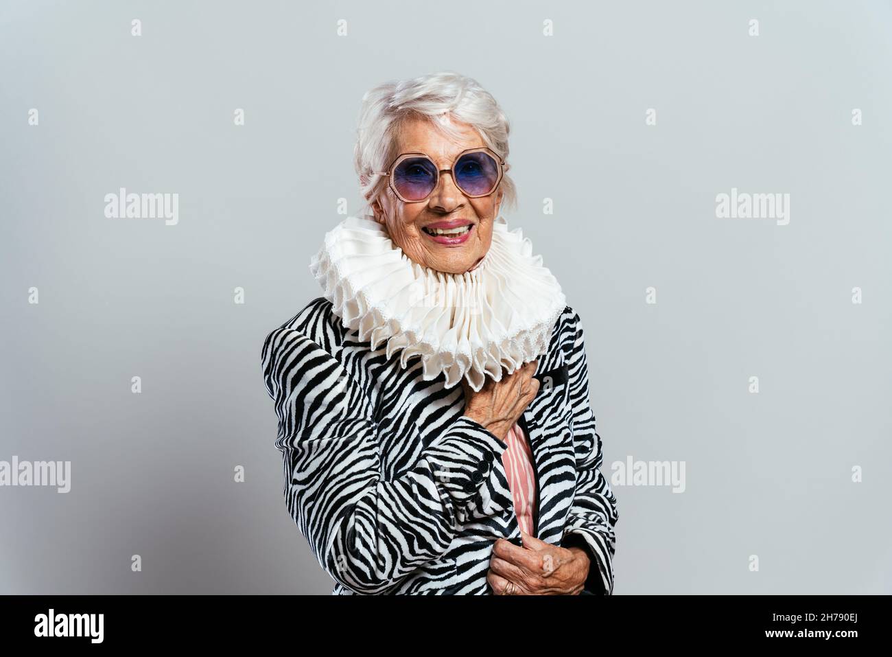 beautiful and elegant old influencer woman. Cool grandmother posing in studio wearing fashionable clothes. Happy senior lady celebrating and making pa Stock Photo