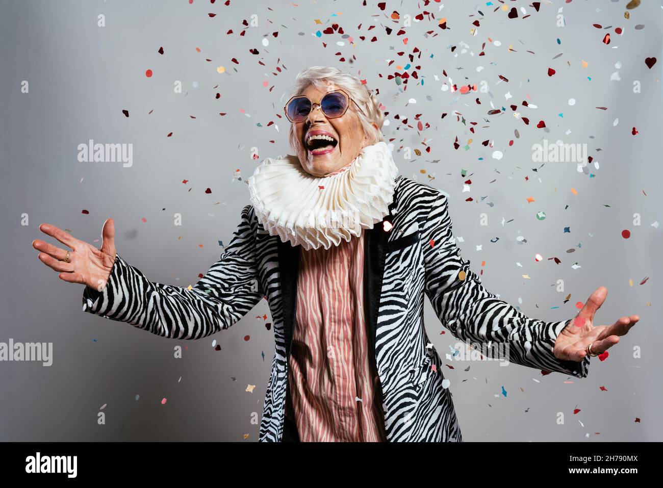 beautiful and elegant old influencer woman. Cool grandmother posing in studio wearing fashionable clothes. Happy senior lady celebrating and making pa Stock Photo