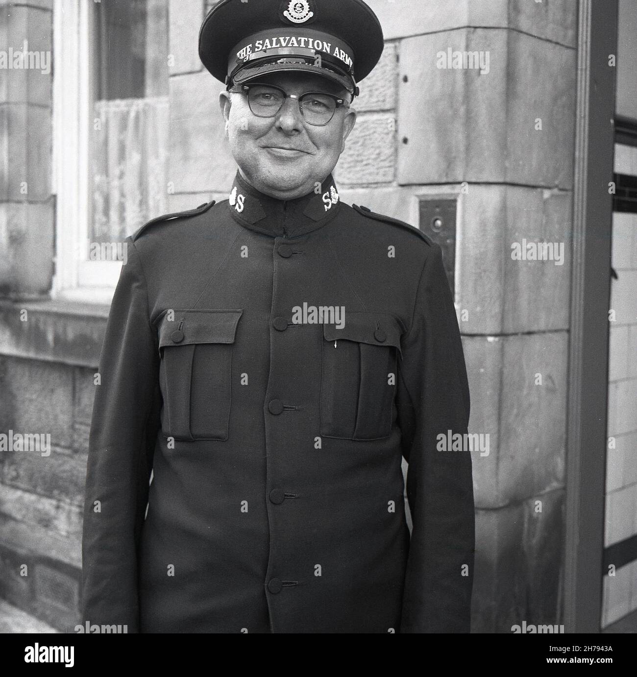 1965, historical, outside a building, a soldier of The Salvation Army in his uniform and hat standing for his photo, Fife Scotland, UK. Soldiers of The Salvation Army are Christians who have undertaken a specific convenant or promise regarding lifestyle and beliefs and wear the uniform as a visible sign of their faith. Officers, Soldiers and Adherents are known as Salvationists. Founded in London in 1865 by William Booth and wife, Catherine as a charity to bring 'Salvation' to the poor & destitute, Booth introduced the military structure in 1878, which continued as a matter of tradition. Stock Photo