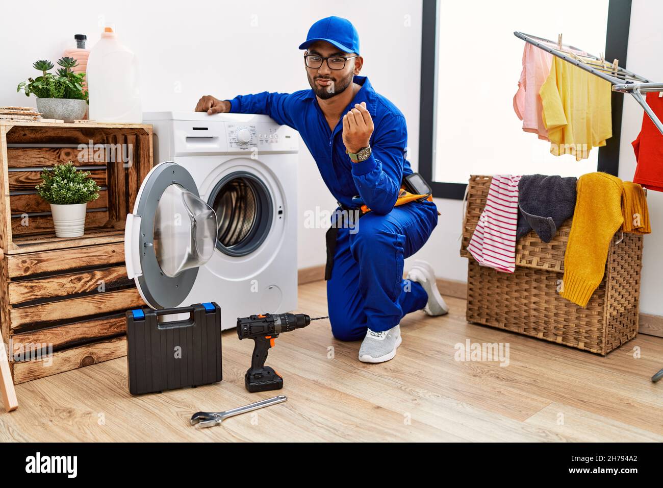 Young indian technician working on washing machine doing money gesture