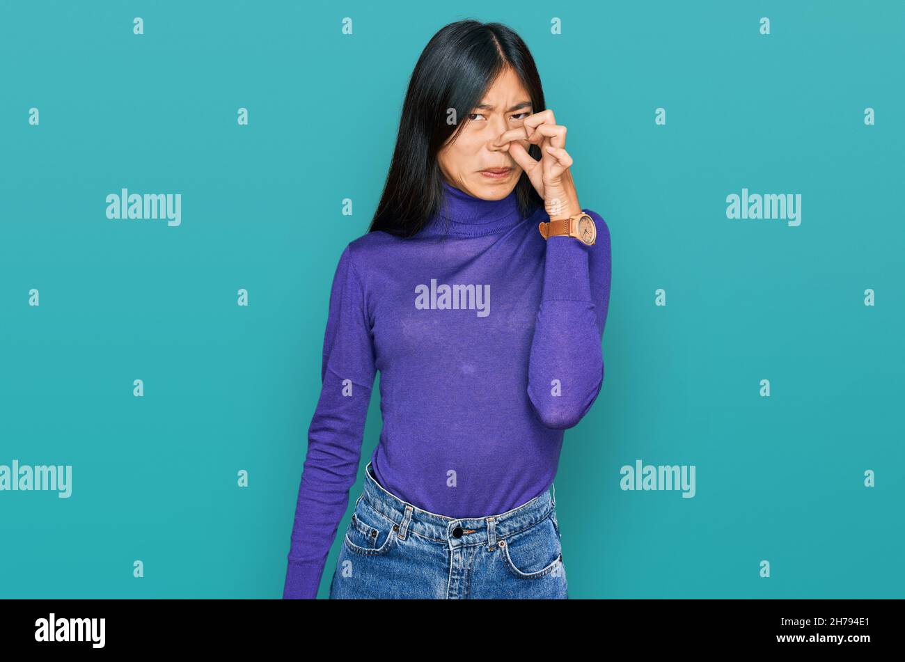 Beautiful young asian woman wearing casual clothes smelling something stinky and disgusting, intolerable smell, holding breath with fingers on nose. b Stock Photo