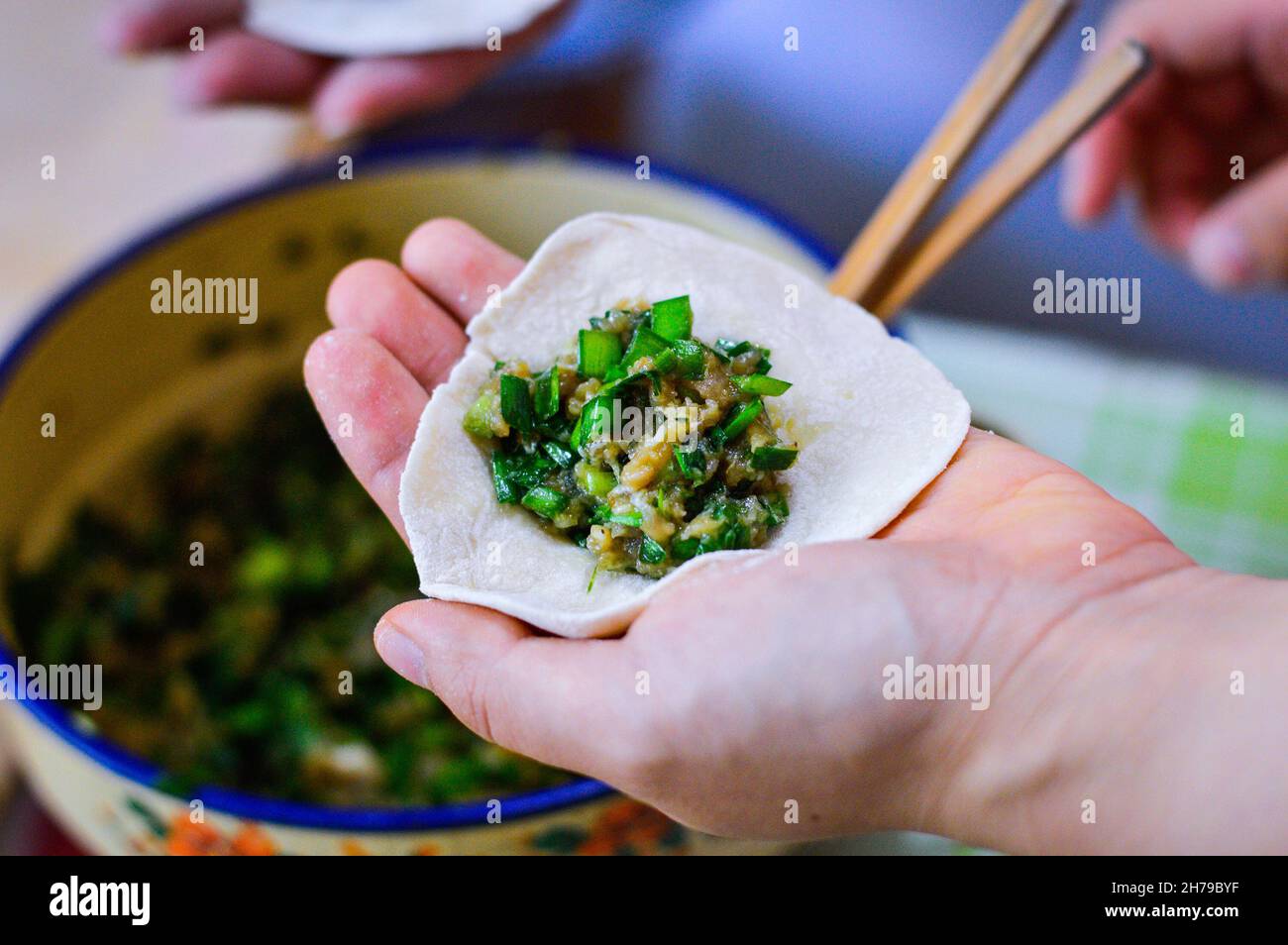 Hand holding Chinese dumpling skin with pork chive filling on top