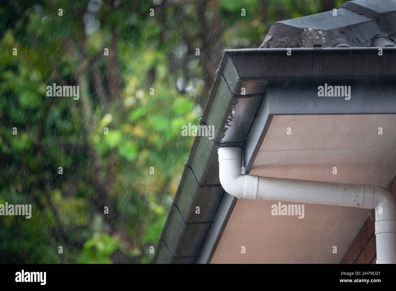 Roof gutter and downpipes in the rain with visible raindrops Stock Photo