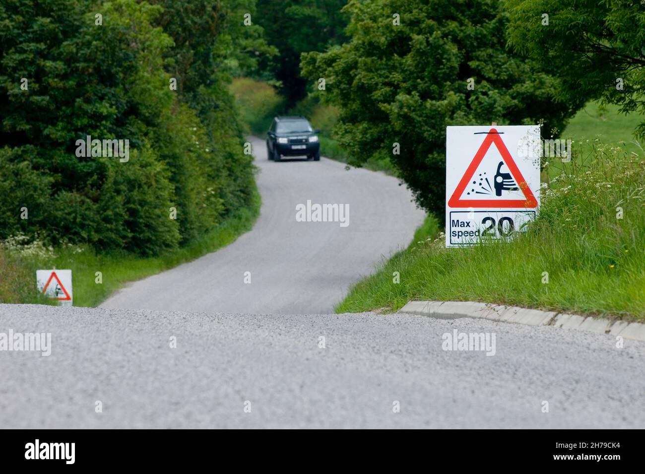 A passenger car approaches a maximum speed 20mph sign on a country B road covered in fresh loose stone chippings, Leicestershire, England, UK. Stock Photo