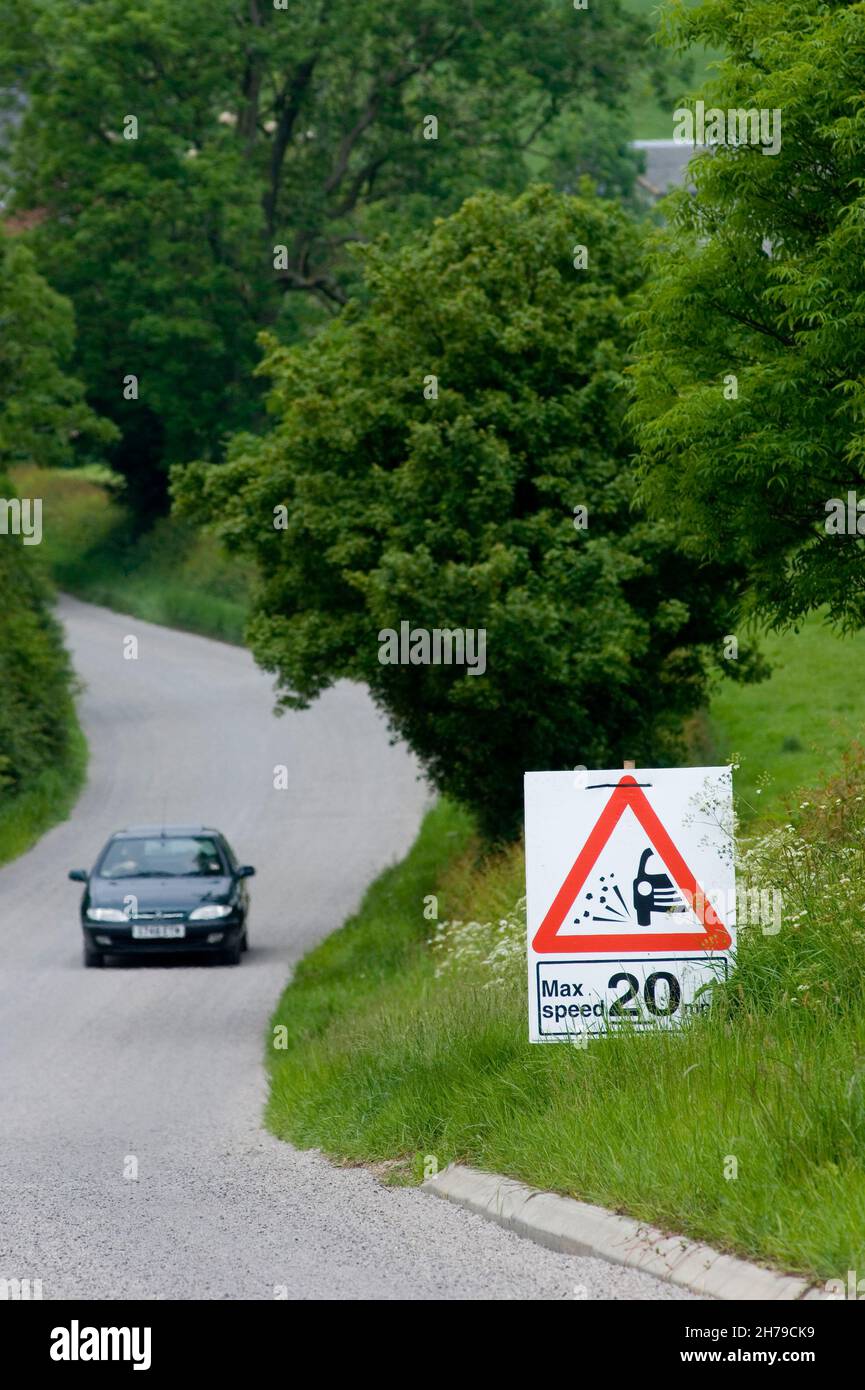 A passenger car passes a maximum speed 20mph sign on a country B road covered in fresh loose stone chippings, Leicestershire, England, UK. Stock Photo