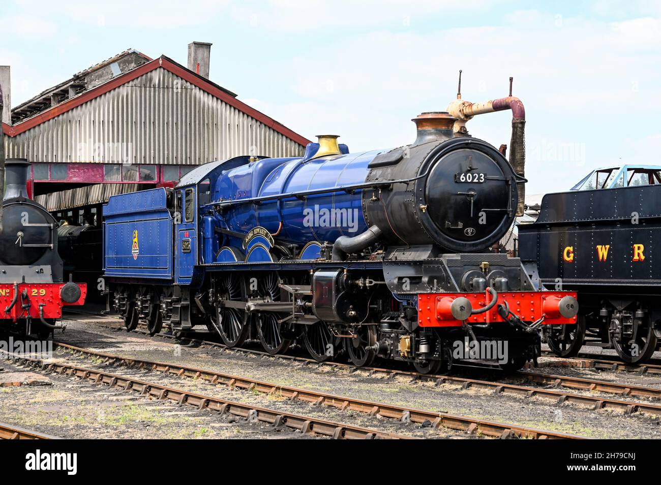 Didcot, England - June 2021: Vintage steam engine outside an engine shed alongside other locomotives Stock Photo