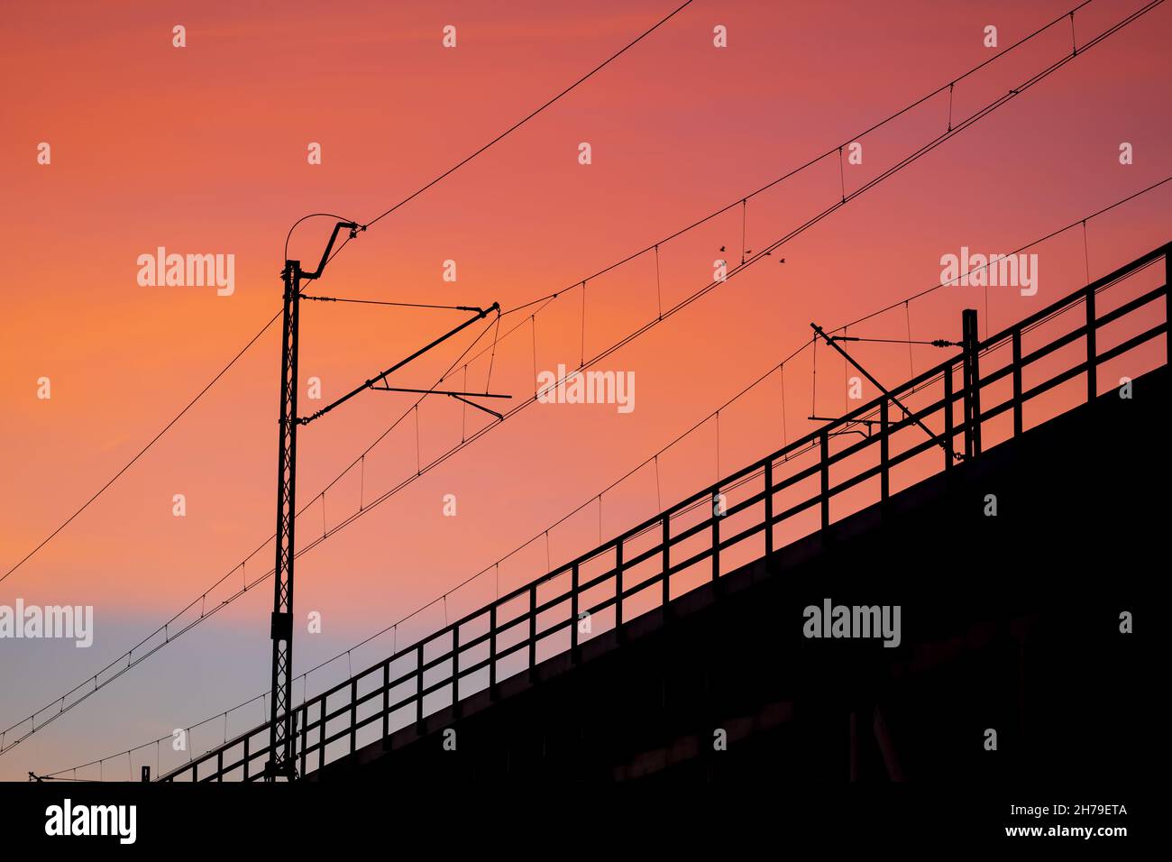 Sunset sky with silhouette of railway bridge electric traction and balustrade. Stock Photo