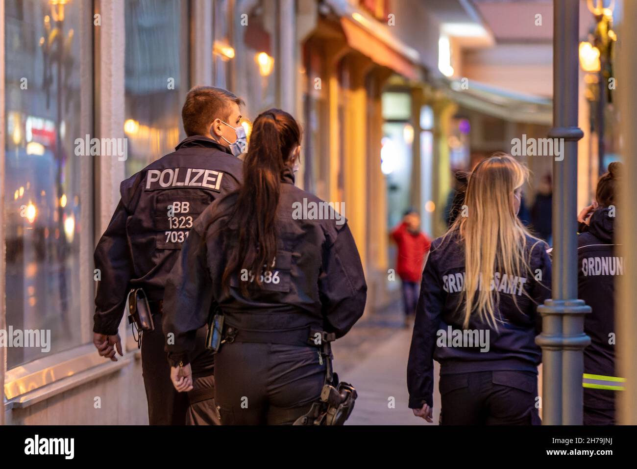 Cottbus, Germany. 19th Nov, 2021. Employees of the public order office and a police officer walk on Berliner Straße. A joint patrol consisting of employees of the public order office and police officers of the Cottbus/Spree-Neiße police inspection checks the enforcement of the provisions of the SARS-CoV-2 containment ordinance in Cottbus city centre. Credit: Frank Hammerschmidt/dpa-Zentralbild/dpa/Alamy Live News Stock Photo