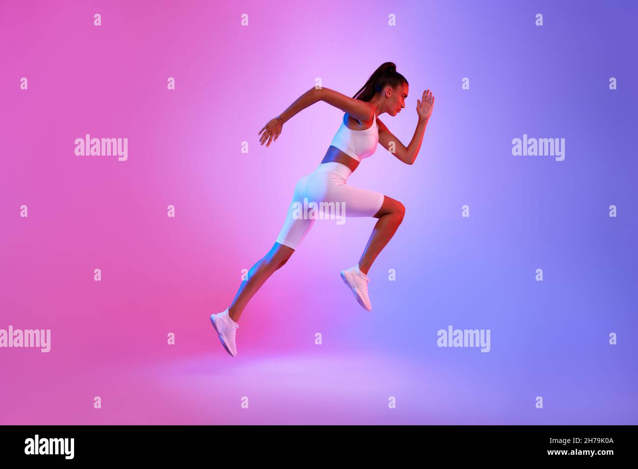 Determined Sporty Woman Running In Mid-Air Over Neon Background, Side-View Stock Photo