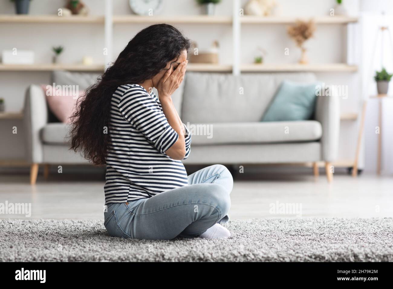 Crying pregnant woman feeling down while staying alone at home Stock Photo