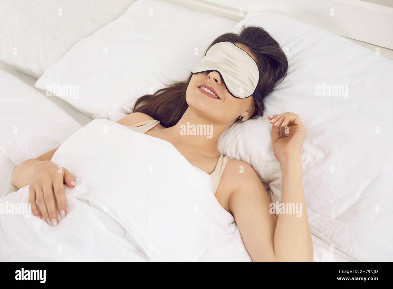 Happy relaxed beautiful young woman wearing an eye mask while sleeping in her bed Stock Photo