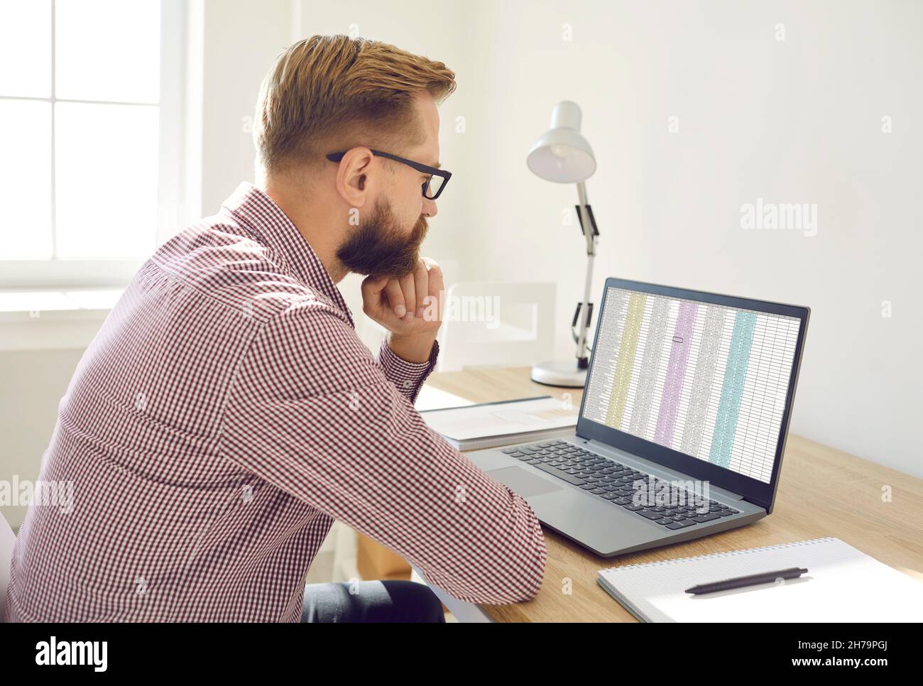 Serious financial accountant looking at spreadsheet on laptop screen and thinking Stock Photo