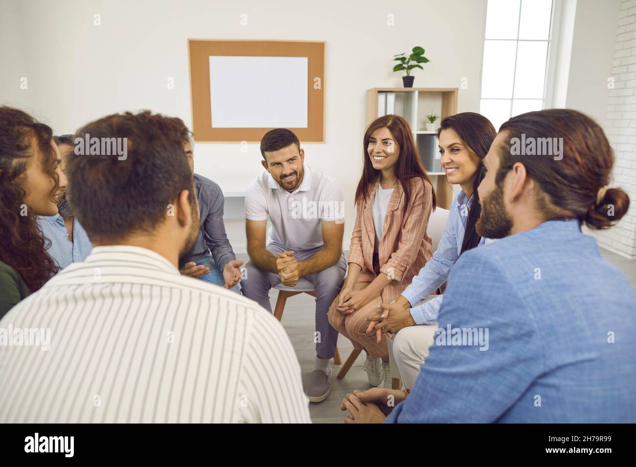 Happy smiling people sitting in a circle and talking during a group therapy session Stock Photo