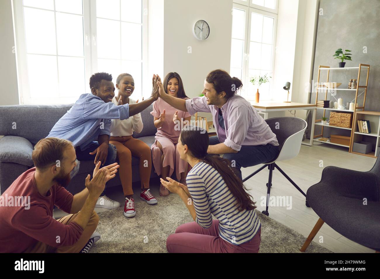 Two interracial men give five to each other while sitting in the company of friends at home. Stock Photo