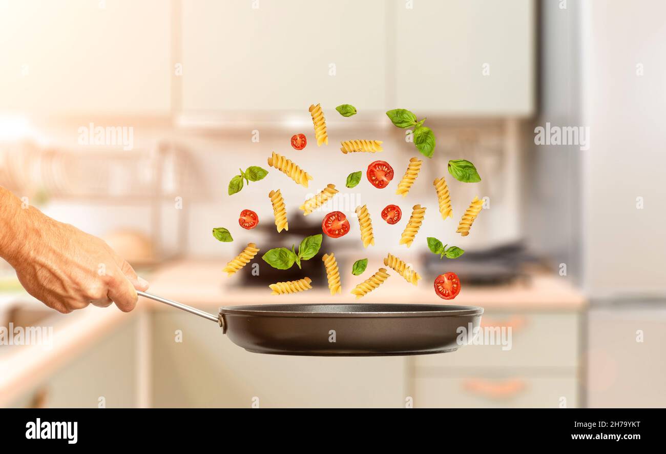 Hand with a frying pan and food on the background of a home kitchen interior. Cooking, groceries, mockup. High quality photo Stock Photo