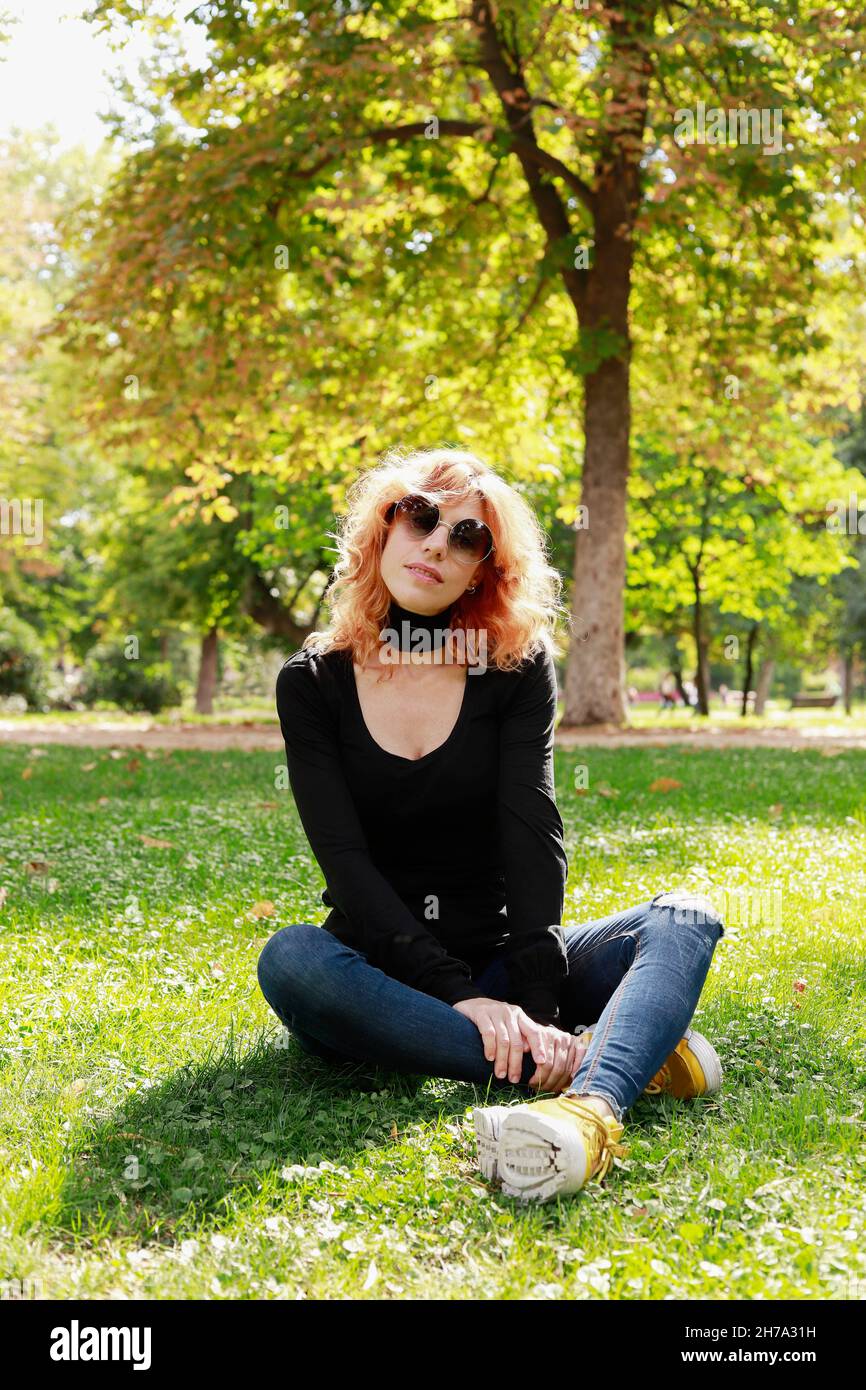 beautiful girl with fashion sunglasses sitting on the lawn looking at the camera Stock Photo