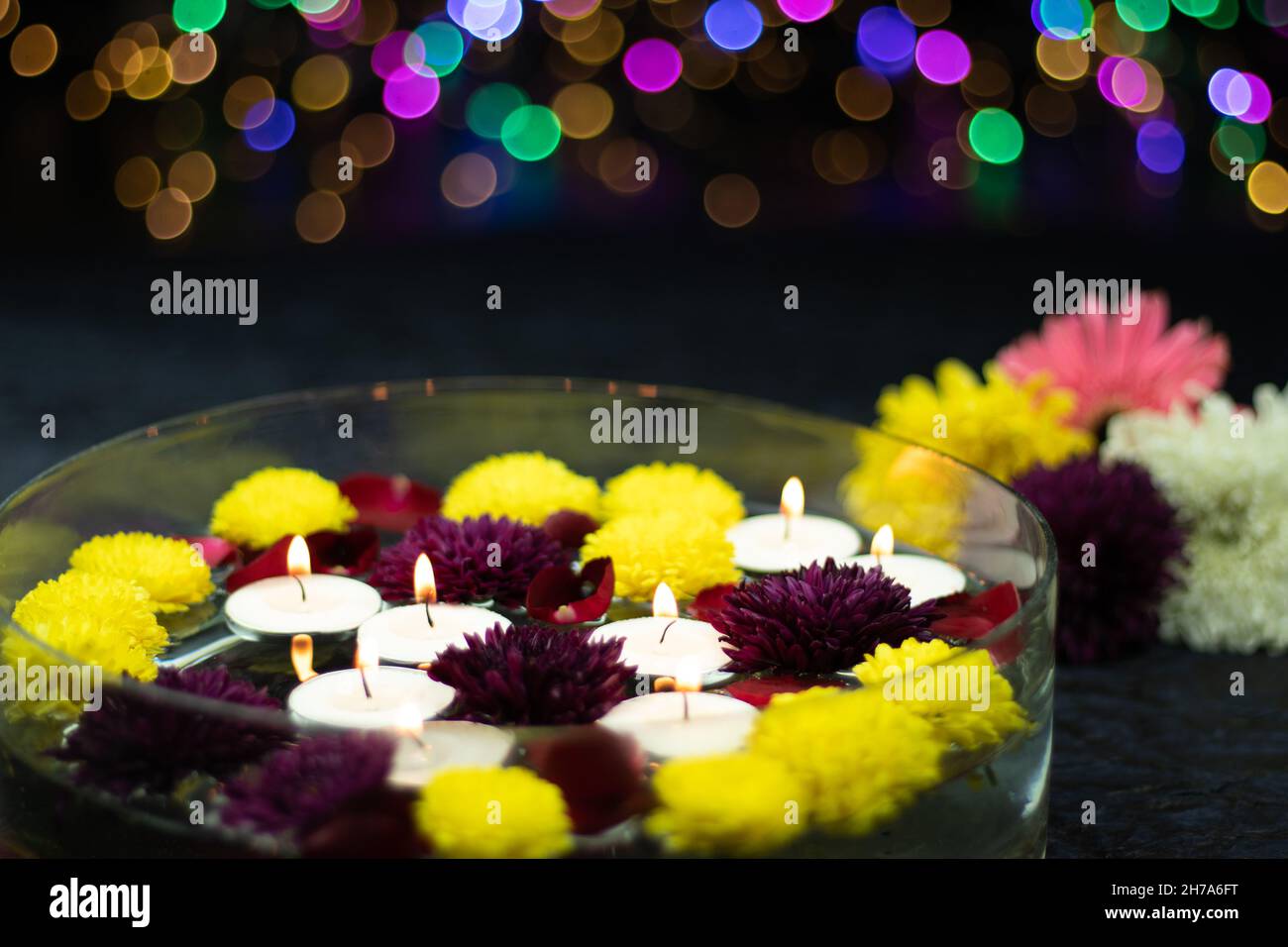 Floating Tealight Candles Illuminated In Decorative Urli Crystal Bowl Filled With Water And Flowers. Colorful Bokeh On Dark Background. Theme For Shub Stock Photo