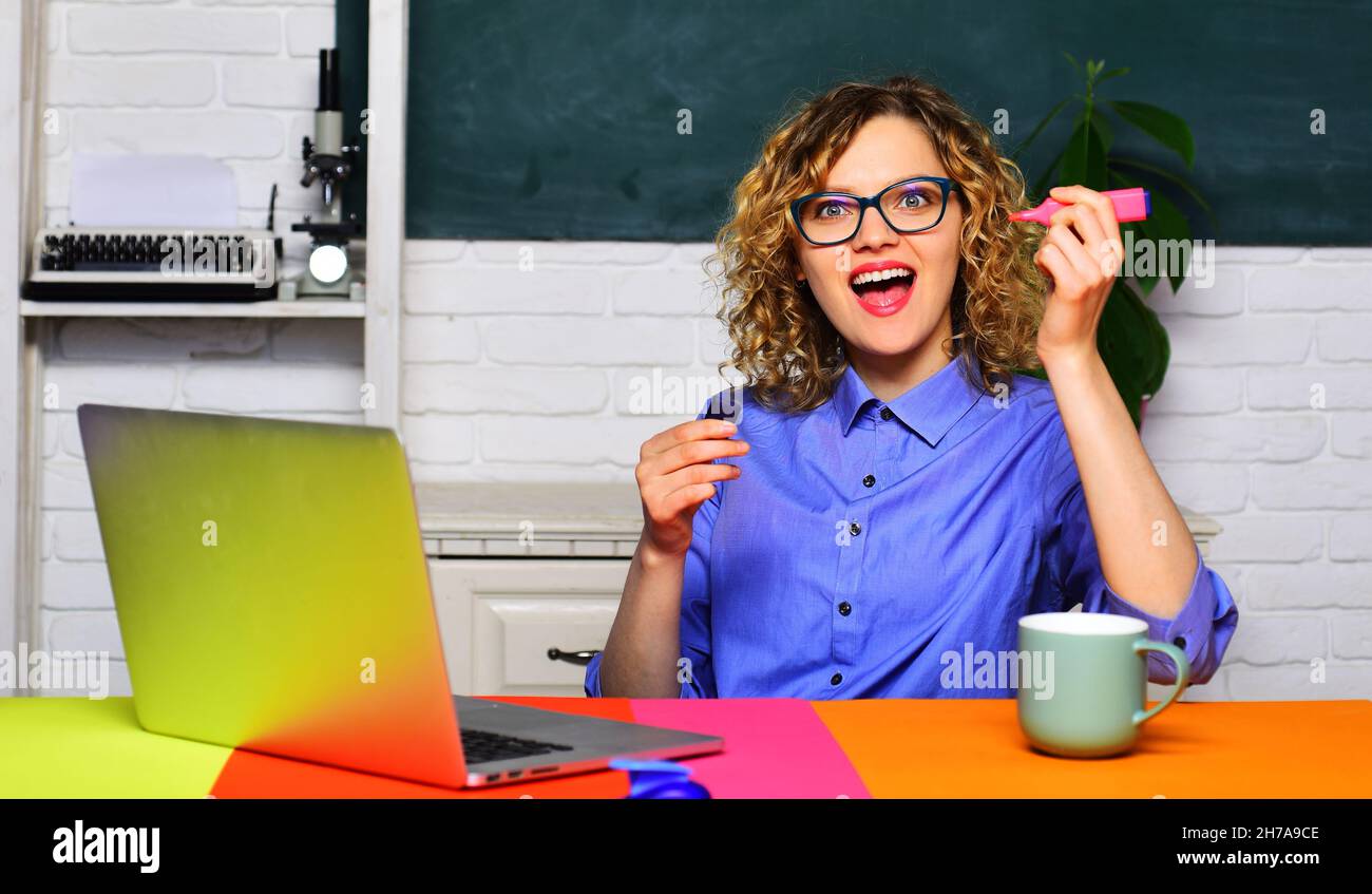 Smiling teacher at desk in classroom. Female student studying in