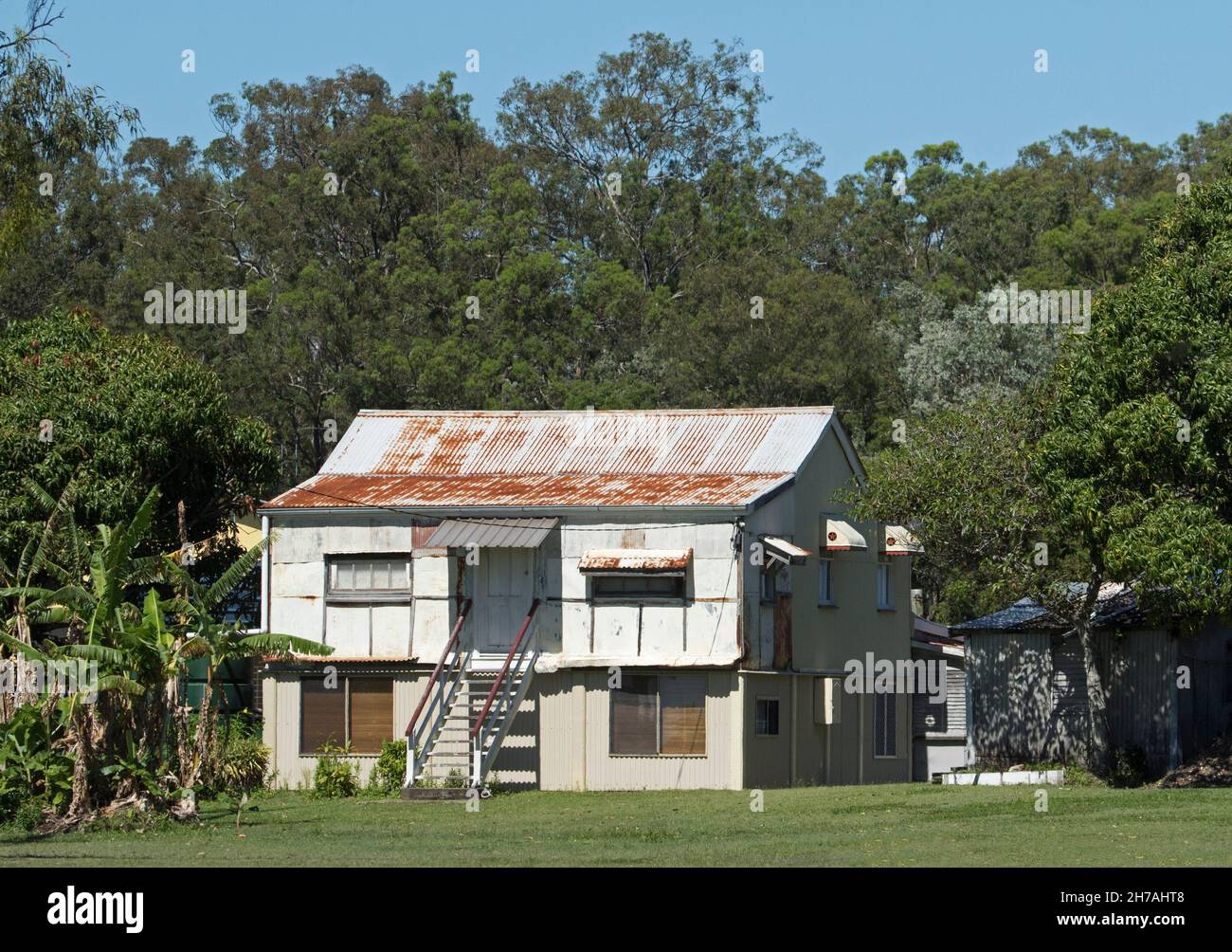 Old dilapidated double storey fibro cottage, fisherman's shack , at coastal town in Australia beside forest of tall trees Stock Photo