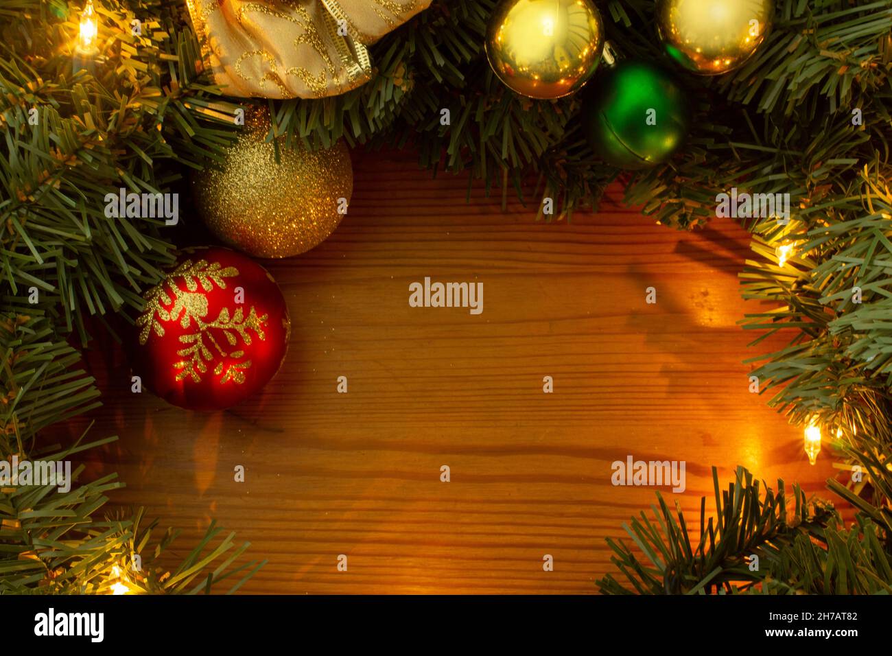 Frame formed by green Christmas tree branches, yellow lights, golden and red light bulbs on a wooden table Stock Photo