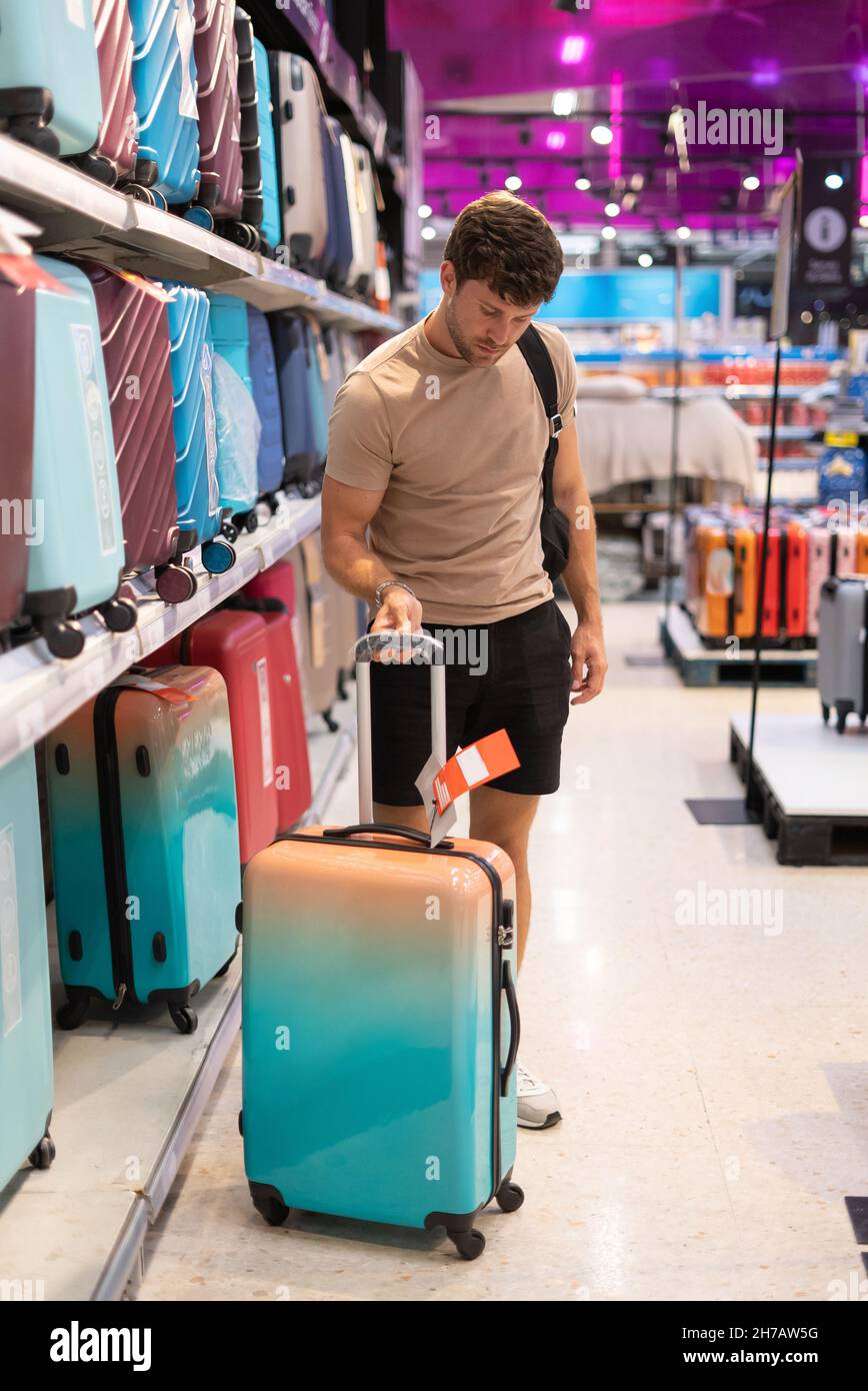 Full body man in t shirt and shorts inspecting modern suitcase while shopping in mall Stock Photo
