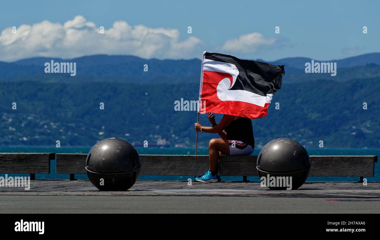 A person sits holding the Tino Rangatiratanga flag, otherwise known as the Maori flag, in Aotearoa, New Zealand. Stock Photo