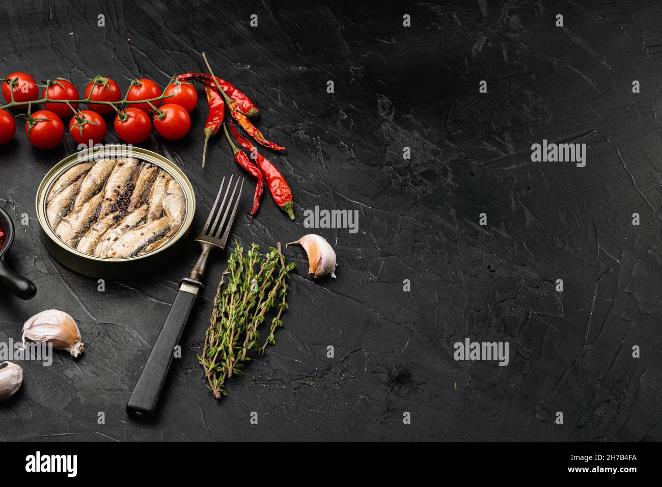 Open can of sprats canned smoked fish set, on black dark stone table ...