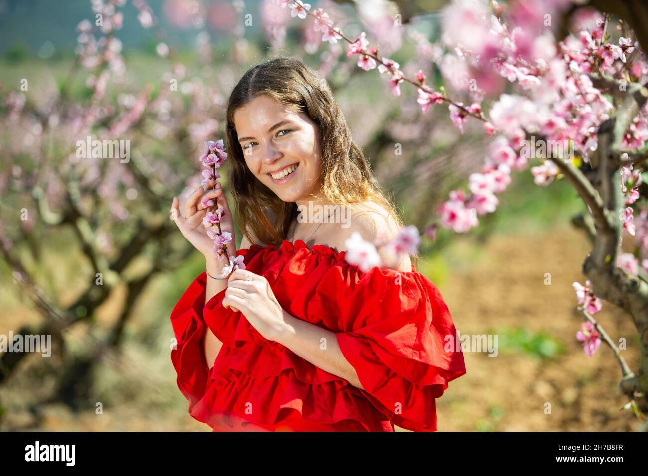 Woman in red dress standing near blooming peach tree Stock Photo